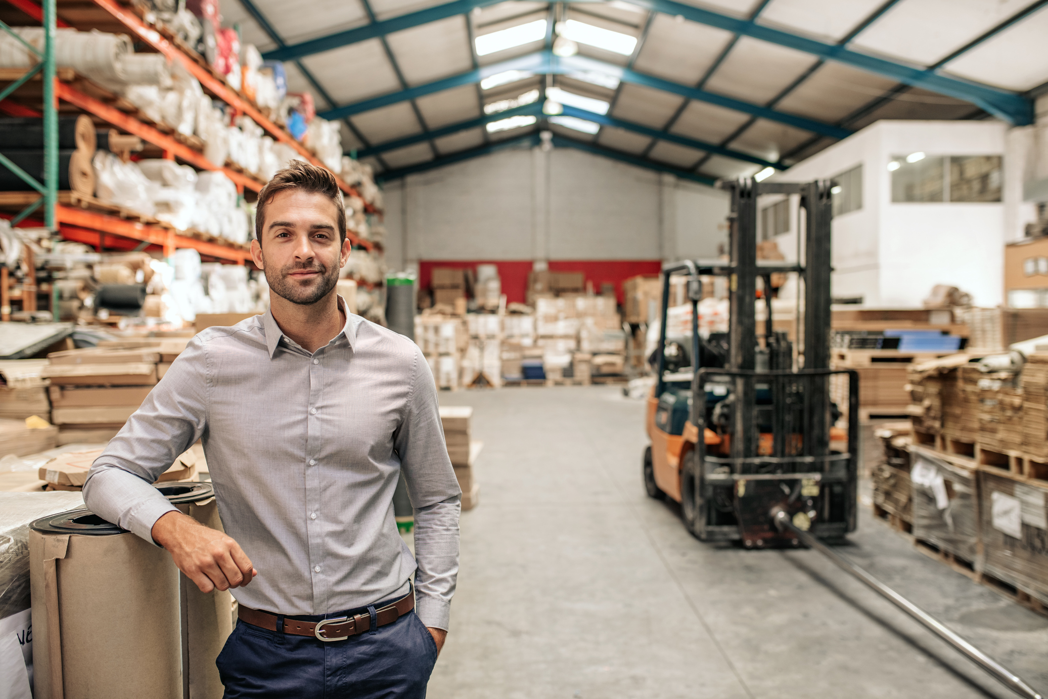 Smiling manager leaning against stock in a large warehouse